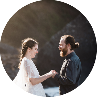 A bride and groom hold hands and grin at each other as they elope on a rocky beach in Northern California
