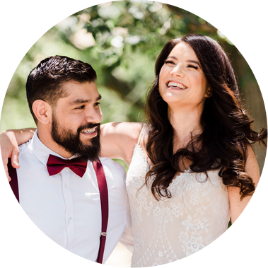 A couple at their wedding, surrounded by trees, jumping up and down with excitement