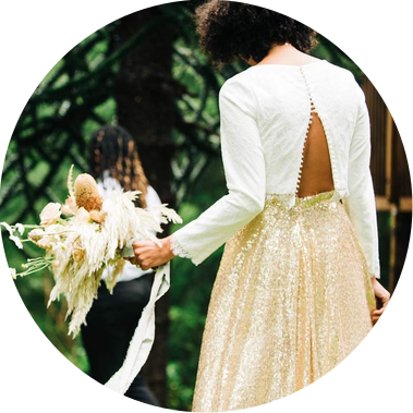 A bride approaches her groom outside of their cabin to show him her wedding outfit