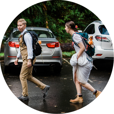 An eloping couple runs through a rainy trailhead parking lot, carrying backpacks