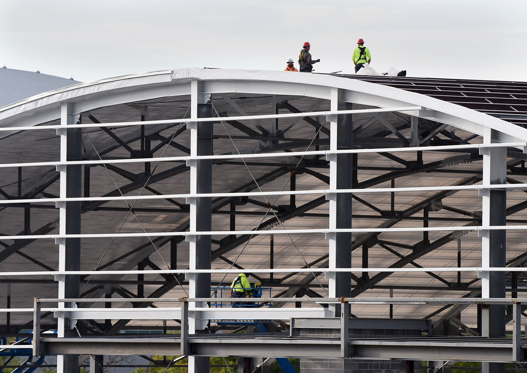 Construction workers stand on the structure they're working on in neon vests and helmets.