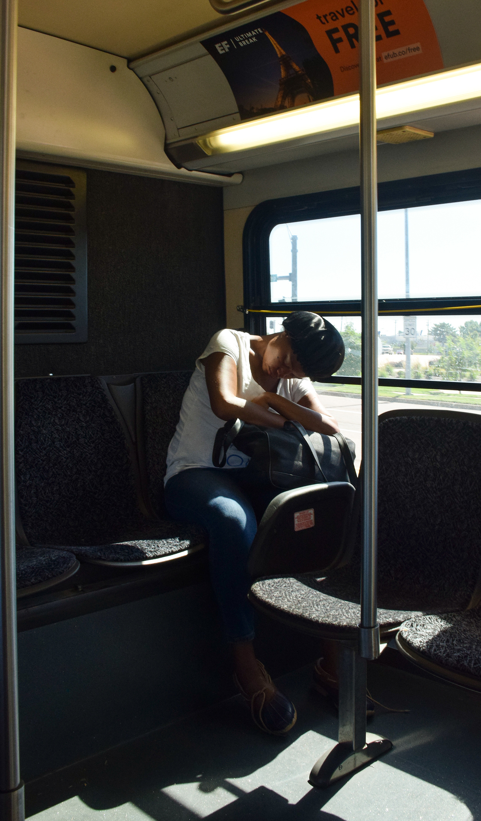A woman rests her head on her backpack and sleeps on the city bus.