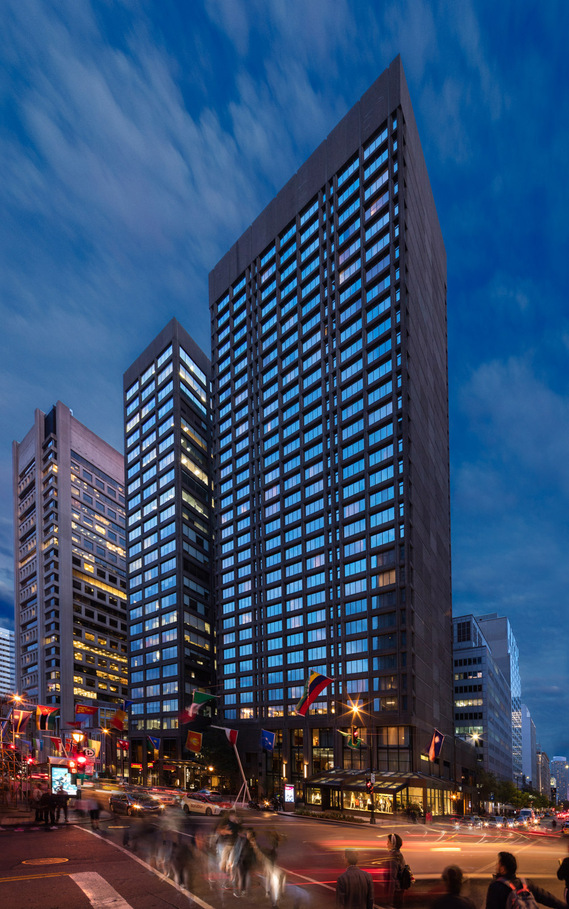 Hôtel Omni, rue Sherbrooke à Montréal photographié au crépuscule du rez-de-chaussée aux étages supérieurs, au premier plan la rue et son activité urbaine, ses ombreux passants et véhicules 