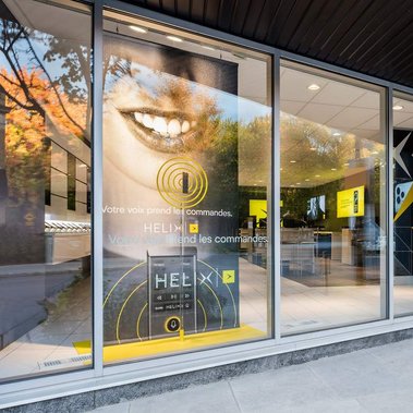 Photo architecturale extérieure de la boutique Vidéotron rue bBeaubien, à Montréal, montrant une grandes affiche publicitaire et les comptoirs de service à l'intérieur