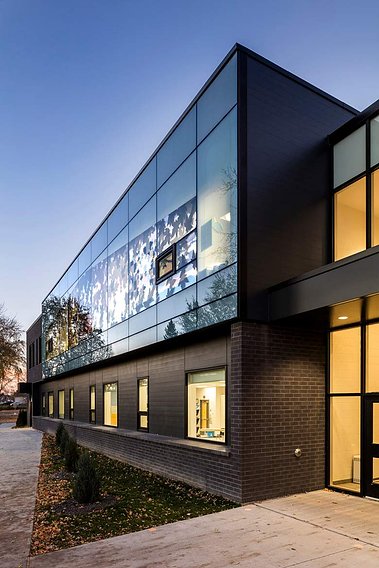 Façade d'une école primaire à la brunante mettant en contraste la luminosité intérieure et le ciel bleu