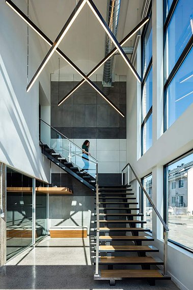 Escalier dans un espace à bureaux à Montréal, grandes fenêtres d'un côté, néons suspendus au plafond, jeune femme descendant les escaliers