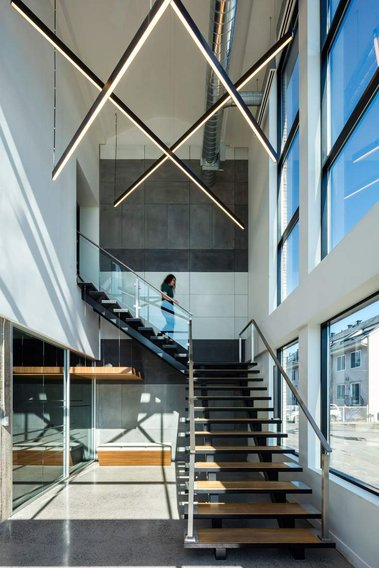Escalier dans un espace à bureaux à Montréal, grandes fenêtres d'un côté, néons suspendus au plafond, jeune femme descendant les escaliers