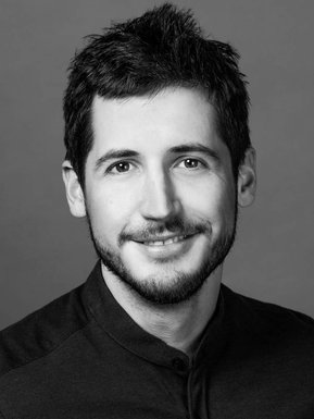 Portrait corporatif en noir et blanc réalisé en studio, jeune homme en tenu décontracté, souriant et portant la barbe