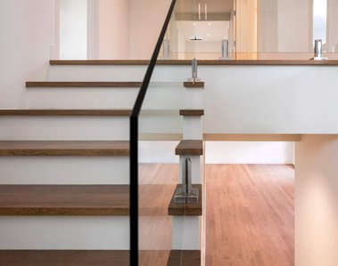 Vue d'une escalier montant à l'étage, vue sur le bois franc du salon non meublé,  et une partie de l'étage, les rampes sont en verre