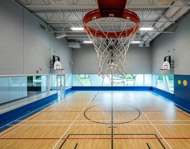 Photo d'architecture intérieure d'un gymnase pour les architectes qui l'ont conçu, vue montrant le plancher et trois murs ainsi qu'un panier de basketball au premier plan