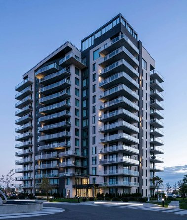 Condos Marquise Phase III, à Laval, vue de sa façade au lever du jour, couleurs bleutées, pavé et fontaine devant l'entrée principale
