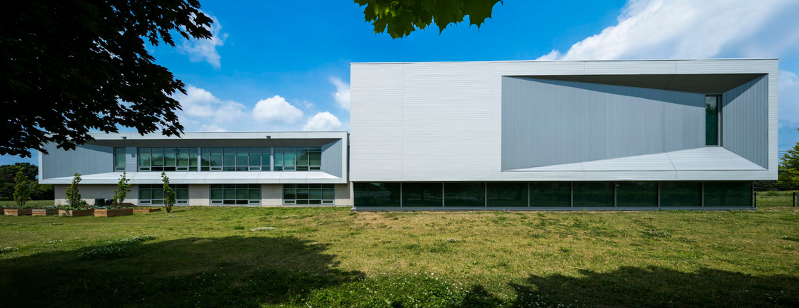 Grande photo panoramique d'une école en plein soleil, encadrés par des feuilles et une vaste pelouse