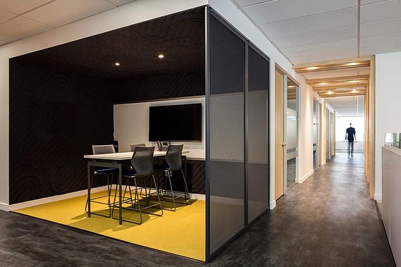 Petite salle de réunion aménagée à la rencontre de deux corridors où on voit  la silhouette d'un homme qui marche