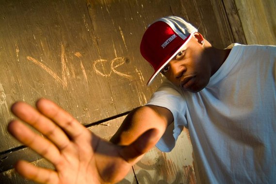 Photo d'un rappeur dans un environnement urbain, la main tendu vers la caméra, une casquette rouge sur la tête