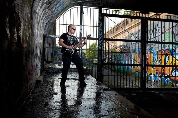 Portrait environnemental d'un musicien sous un viaduc à Montréal, jouant de la guitare devant une grande grille