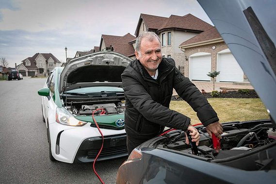 Service de survoltage des batteries offert par COOP Taxi, le chauffeur survolte une batterie de voiture, la sienne est visible à l'arrière plan