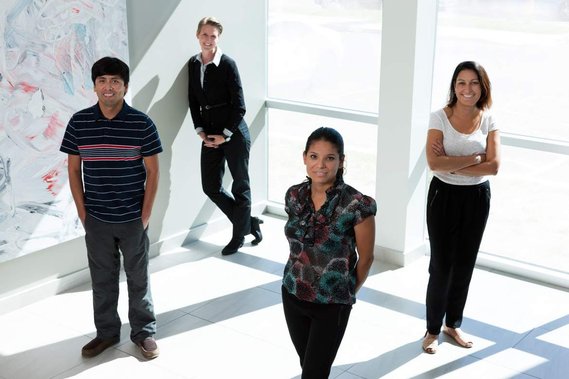 Photo corporative d'un petit groupe d'employés, à la réception de leur entreprise, debout devant une fenêtre laissant entrer la lumière vive du soleil