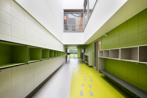 Photo d'architecture intérieure d'un corridor dans une école avec ses couleurs vives, ses espaces de rangement pour les vêtements des élèves, et sur le plancher des dessins de pas comme décoration