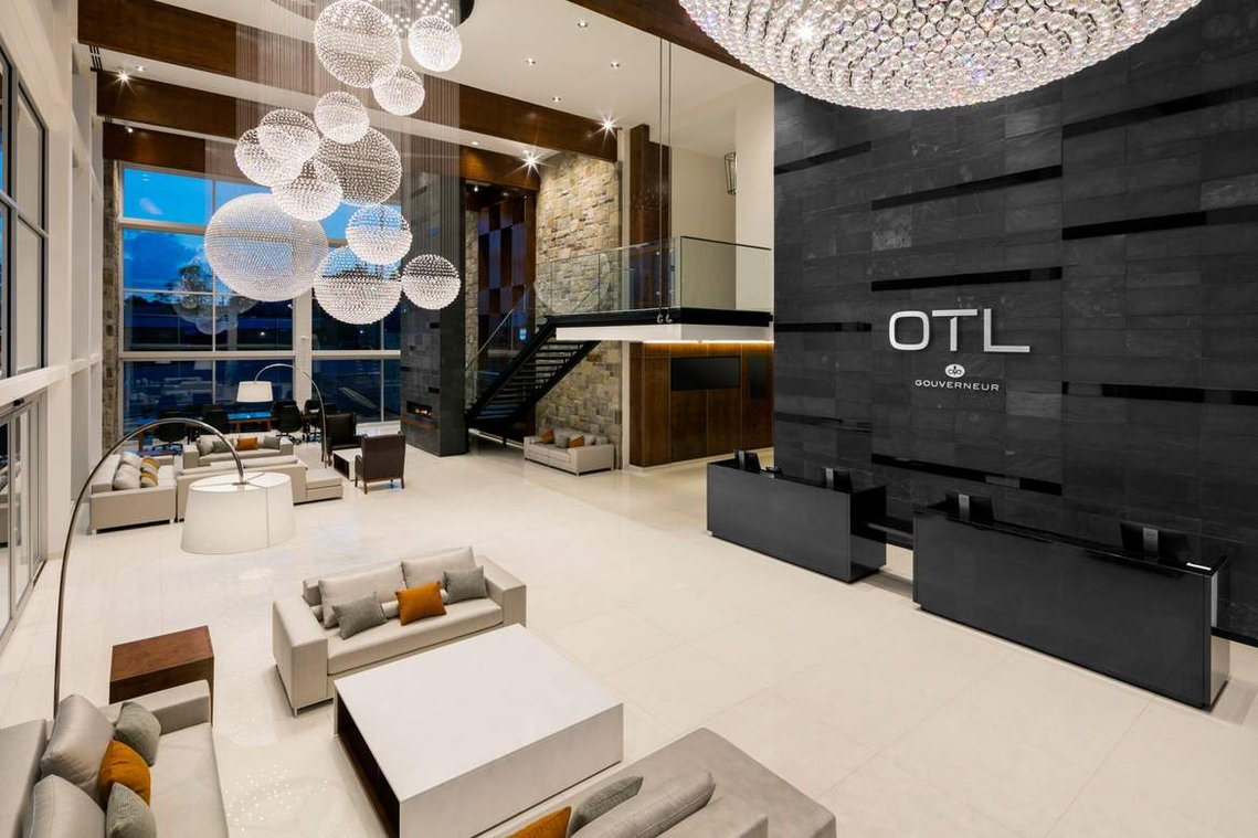 Lobby de l'hôtel OTL à Sherbrooke, montrant son logo au dessus du bureau de réception, des espaces lounge avec de vastes canapés, ainsi qu'un spectaculaire luminaire constitué de millier de petites billes de verres formant plusieurs grandes sphères