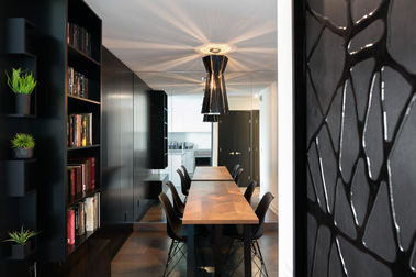 Condo à l'Ile des Soeurs à Montréal avec sa longue table de cuisine et une bibliothèque en bois noir d'un côté et l'espace cuisine à l'arrière plan