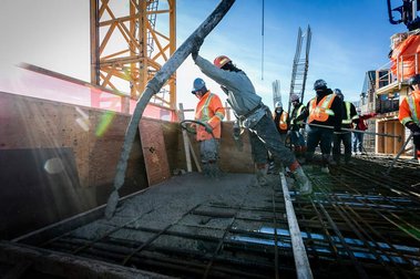 Ouvrier manipulant un énorme boyau crachant du béton liquide sur chantier de construction