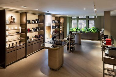Boutique Nespresso rue Peel à Montréal, vue du deuxième étage, montrant les présentoirs de produits, les plantes vertes et fenêtres donnant sur la rue
