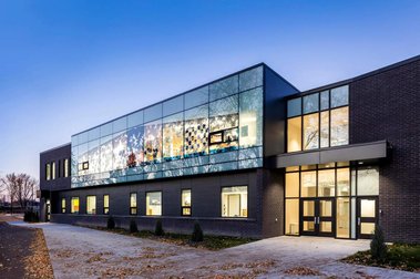 Façade d'une école primaire photographiée au crépuscule montrant ses murs extérieurs de brique noire et ses grandes fenêtres
