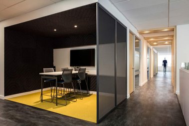 Couloir dans un espace à bureau avec personne floue à l'arrière plan, petite salle de réunion à l'avant plan