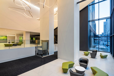 Photo architecturale du lobby d'un édifice public montrant deux niveaux, des meubles et une vue sur la rue et la ville de Montréal
