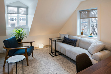 Sale de rencontre d'une clinique de soins psychologiques, fauteuil gris pâle, chaise en tissu bleu, tables à cafés et grandes lucarnes