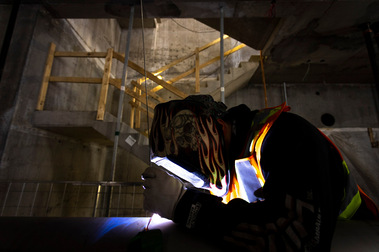 Soudeur masqué en action sur un chantier de construction, derrière lui un escalier en béton sécurisé par des rampes en bois