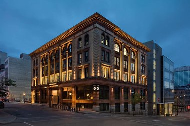 Édifice du 7 St-Jacques ouest, à Montréal photographié au crépuscule, montrant sa façade éclairée mettant en vedette ses grandes fenêtres en arches