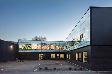 Façade arrière d'une école primaire entourant une cours de récréation,  elle montre les grandes surfaces vitrées de son architecture ainsi que les murs de brique noire