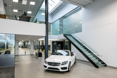 Photo d'architecture intérieure du concessionnaire automobile Mercedes-Benz Rive-Sud montrant une véhicule et un grand escalier montant à l'étage ainsi que les espaces de service à la clientèle