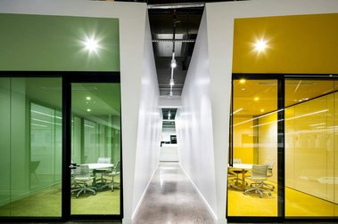 Petit couloir dans un espace à bureaux avec de part et d'autre deux petites salles de réunion dont les vitrines sont vertes et jaunes