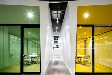 Petit couloir dans un espace à bureaux avec de part et d'autre deux petites salles de réunion dont les vitrines sont vertes et jaunes
