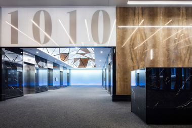 Lobby d'un édifice à bureaux, montrant une partie du bureau de la sécurité ainsi que l'accès aux ascenseurs située sous un plafond de lattes de bois et de néons.