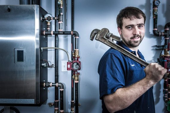 Portrait éditorial d'un plombier dans son milieu de travail, avec ses outils, devant des tuyaux