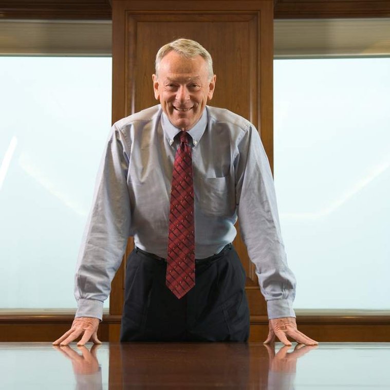 Portrait d'un dirigeant d'entreprise appuyé sur une longue table de conférence avec des fenêtres à l'arrière plan