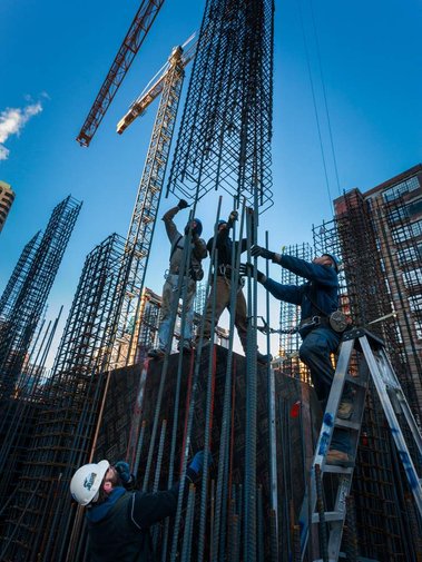 Photo d'ouvriers à l'oeuvre sur un chantier de construction charpentes  de tiges de béton assemblées avant la coulée du béton grue jaune et ciel bleu 