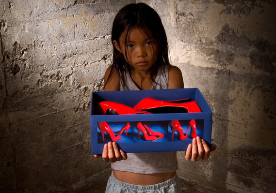 Photo d'une enfant asiatique posant avec des souliers qu'elle aurait confectionnés, photographiée dans un sous-sol
