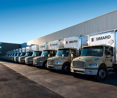 Camions de la compagnie Simard transport alignés face à leurs garages