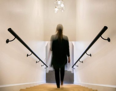 Jeune femme vue de dos descendant un escalier avec de grandes rampes de bois de part et d'autre