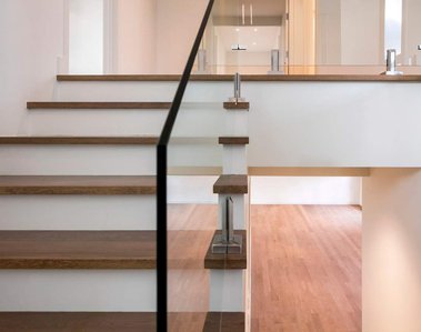 Vue intérieure d'une résidence avec un escalier menant à l'étage, les rampes de verre et le salon au plancher de bois franc 