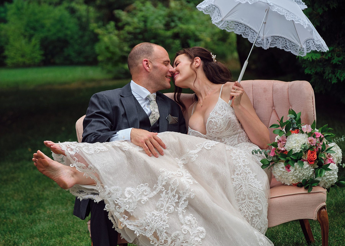Bride and groom photographed under a lace parasol during a brief rain shower.