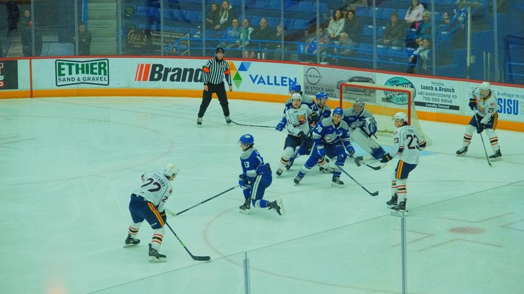 Sudbury wolves hockey players in blue shirts defending against the Barrie colts in white shirt. 
