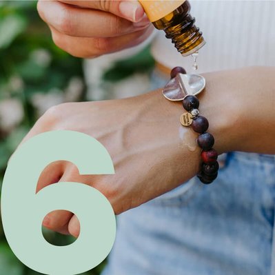 Woman dripping essential oil on bracelet with number 6 for the day of deal we are on.