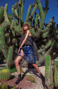 A powerful and elegant woman, captured  by Anrike Piel, poses amidst a striking Barcelona landscape filled with cacti, showcasing high-end fashion and confidence.