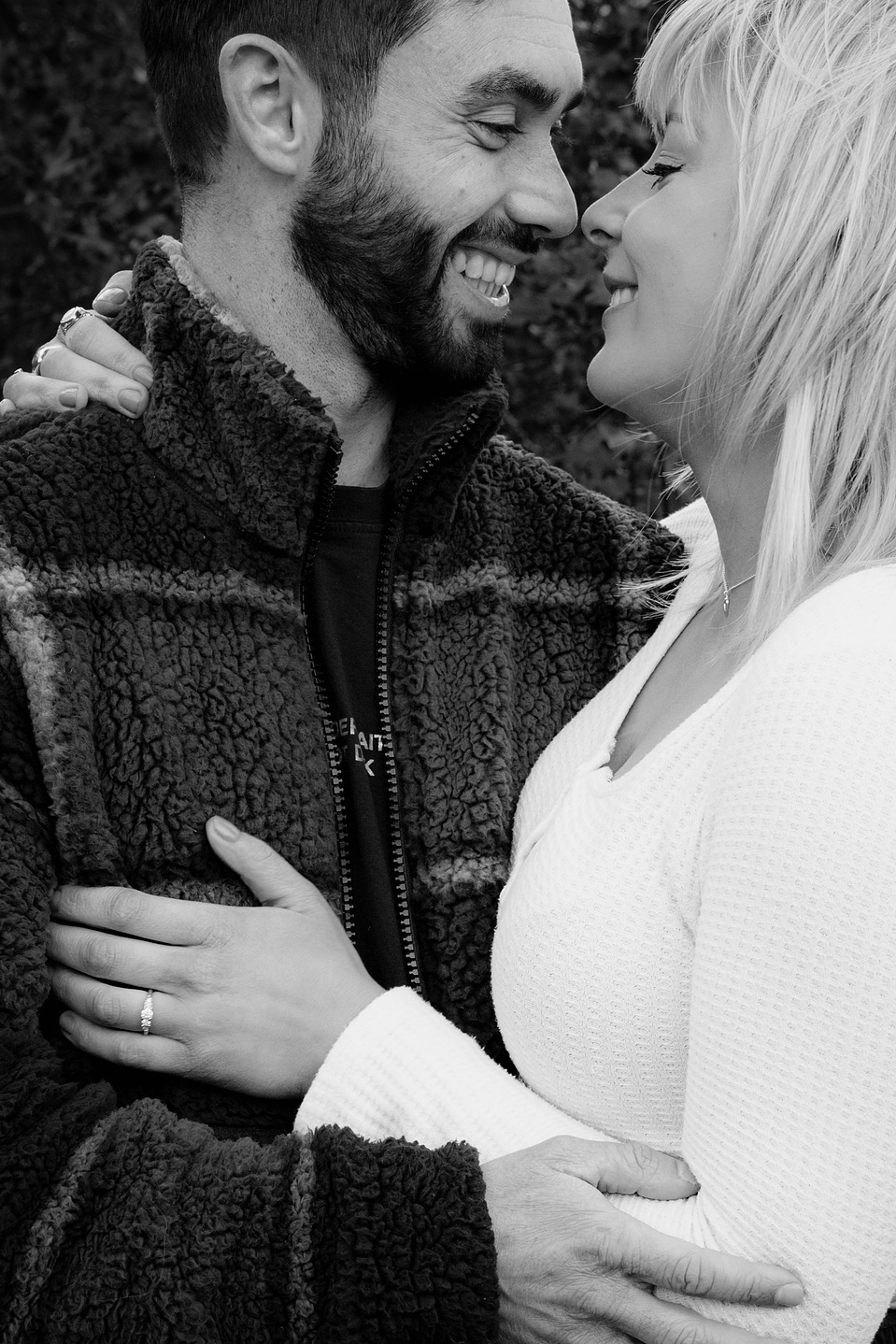 Couple looking at each other and embracing and smiling. Her hand is placed on his chest and showing her new engagement ring.