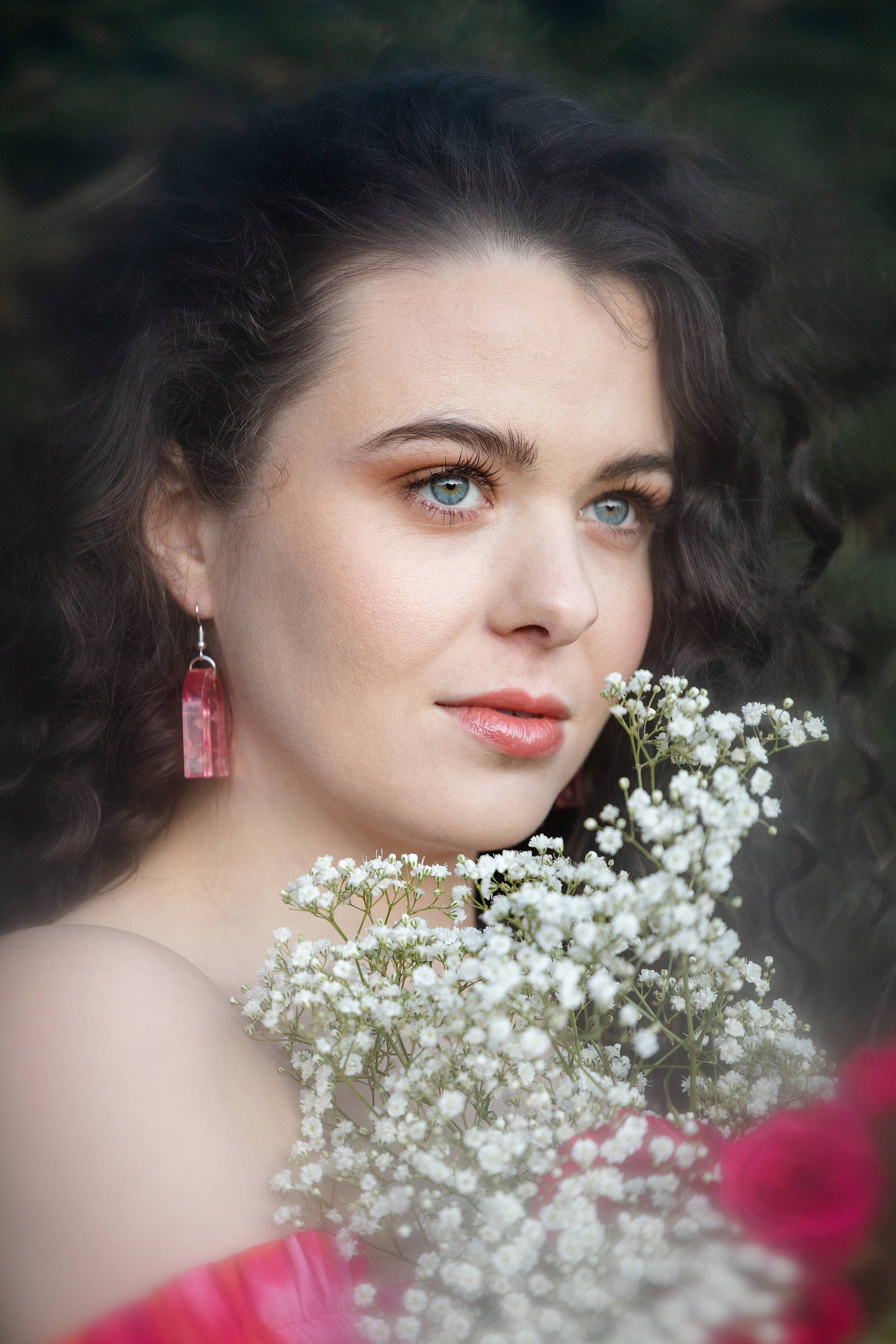 Girl in a pink dress and pink earrings holding some flowers looking out to the distance. Hazy and dream like. 
